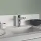 Küchenarmatur mit einem hohen, schwenkbaren Auslauf in Chrom-Finish, montiert auf einer weißen Arbeitsplatte, neben einer schwarzen Schüssel und einem Behälter mit Utensilien. Ideal Standard.